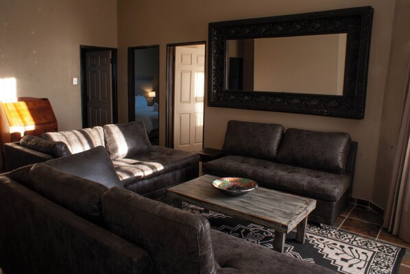A living room with two dark brown leather sofas, a wooden coffee table with a colorful bowl, and a large mirror on the wall.
