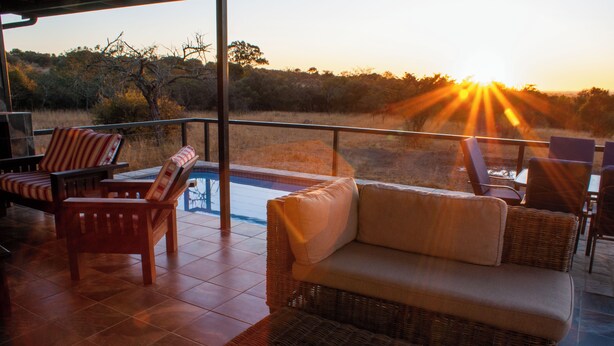 Une terrasse meublée de mobilier en osier, une piscine et une vue sur le coucher du soleil.