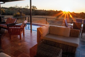 A terrace with wicker furniture, a pool, and a view of the sunset.