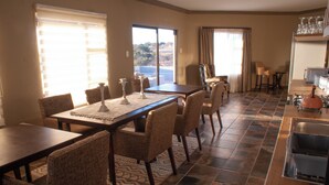 Un coin repas avec une table dressée pour quatre personnes, entourée de chaises en osier, et un espace cuisine comprenant un évier et un plan de travail.