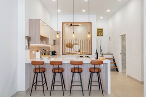 A modern kitchen with a central island, bar stools, pendant lighting, and a visible staircase. - TRES PINOS APARTMENT (Mijas)