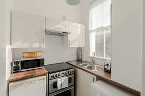 A compact kitchen with white cabinets, a microwave, a stove, and a sink. - Queen's Park 2-Bed Apartment · Sleeps 4 (London)