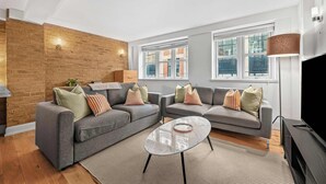 A modern living room with two grey sofas, a glass coffee table, and a brick accent wall. - Elegant Soho 1-Bed - Balcony, 2 Baths, Sleeps 4 (London)
