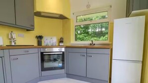 Une cuisine avec des meubles gris, un réfrigérateur blanc et une fenêtre donnant sur un paysage verdoyant.