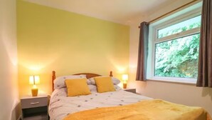 Une chambre à coucher avec un lit, deux lampes de chevet, une fenêtre avec des rideaux et une vue sur la verdure à l’extérieur.