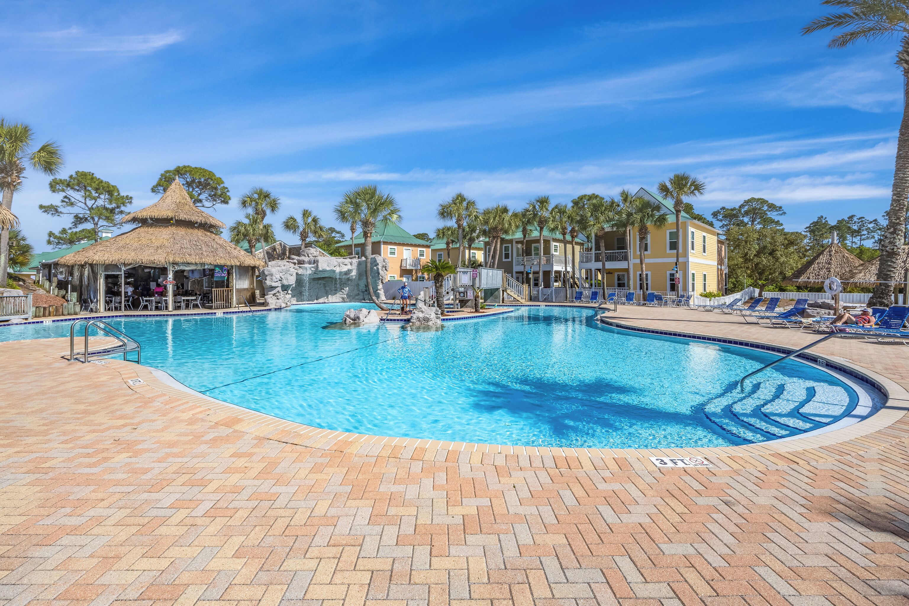 A swimming pool with a brick deck, lounge chairs, and a thatched-roof structure.