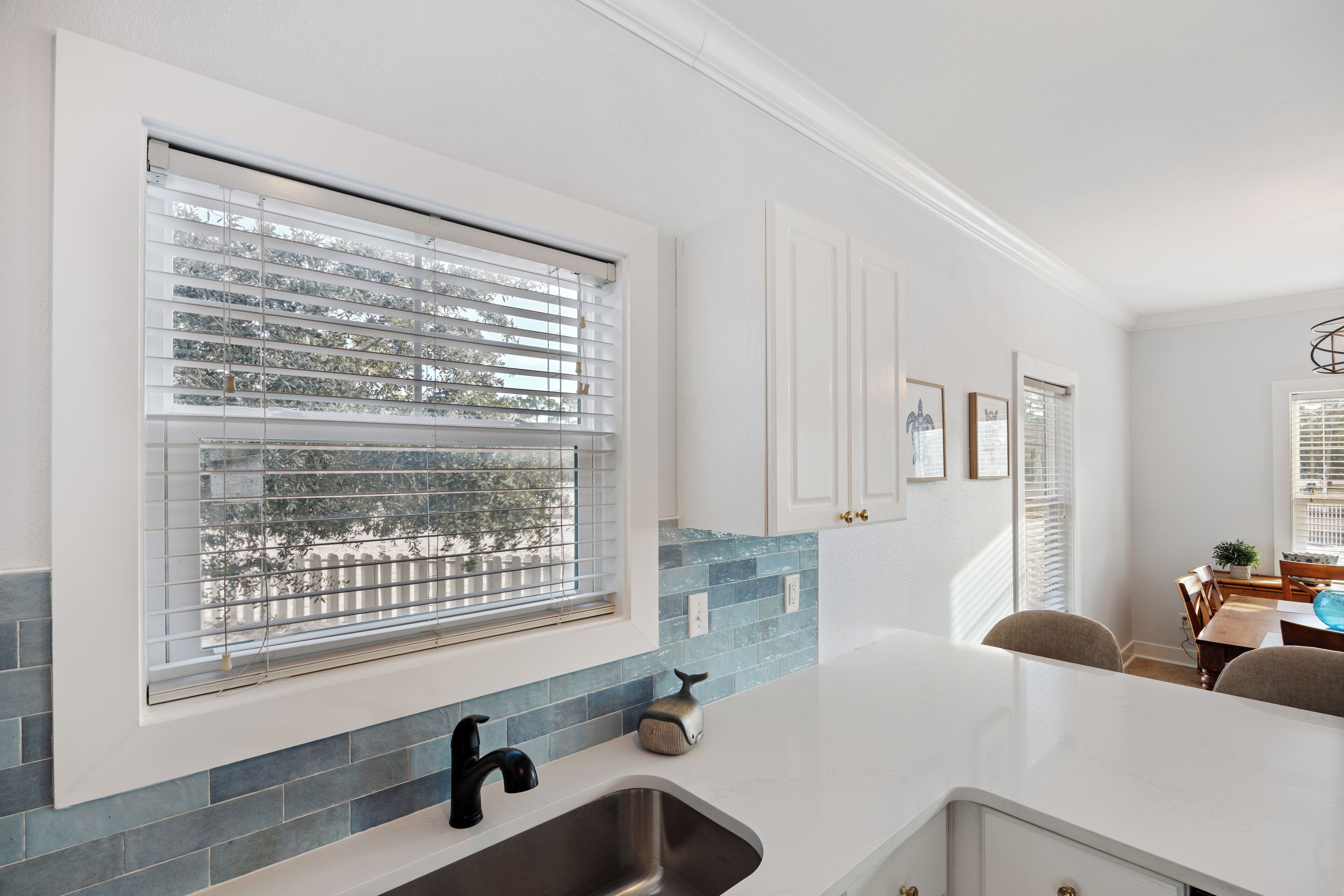 Una cocina con un amplio ventanal, armarios blancos y un salpicadero de azulejos azules.