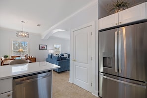 A modern kitchen with a stainless steel refrigerator, a dining area with a table and chairs, and a living room with a sofa and a lamp. - New Purple Parrot Resort Listing! 3 BR With Fully Updated Kitchen and Baths! (Pensacola)