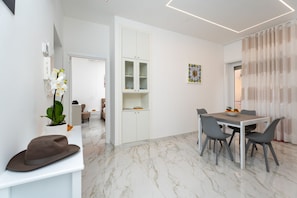 Ein modernes Interieur mit Marmorboden, einem Essbereich mit grauen Stühlen, einem weißen Schrank mit Glastüren und einer Pflanze.