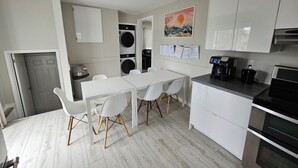 Et moderne køkken med hvide skabe, et spisebord med stole, en kaffemaskine og en vaskemaskine.