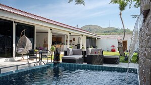 Ein Swimmingpool mit Sitzgelegenheiten im Freien, einer überdachten Terrasse und Blick auf eine hügelige Landschaft.