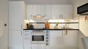 A compact kitchen with white cabinets, a built-in oven, a microwave, and a sink. - Hertford Flat 13 (London)