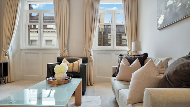 A living room with a glass coffee table, two sofas, and a view of buildings through large windows. - Hertford Flat 13 (London)