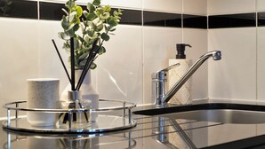 A modern kitchen with a stainless steel sink, a glass tray with a white mug and a plant, and a black soap dispenser. - Hertford Flat 13 (London)