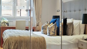 A bedroom with a bed, bedside table, and a window with curtains. - Hertford Flat 13 (London)