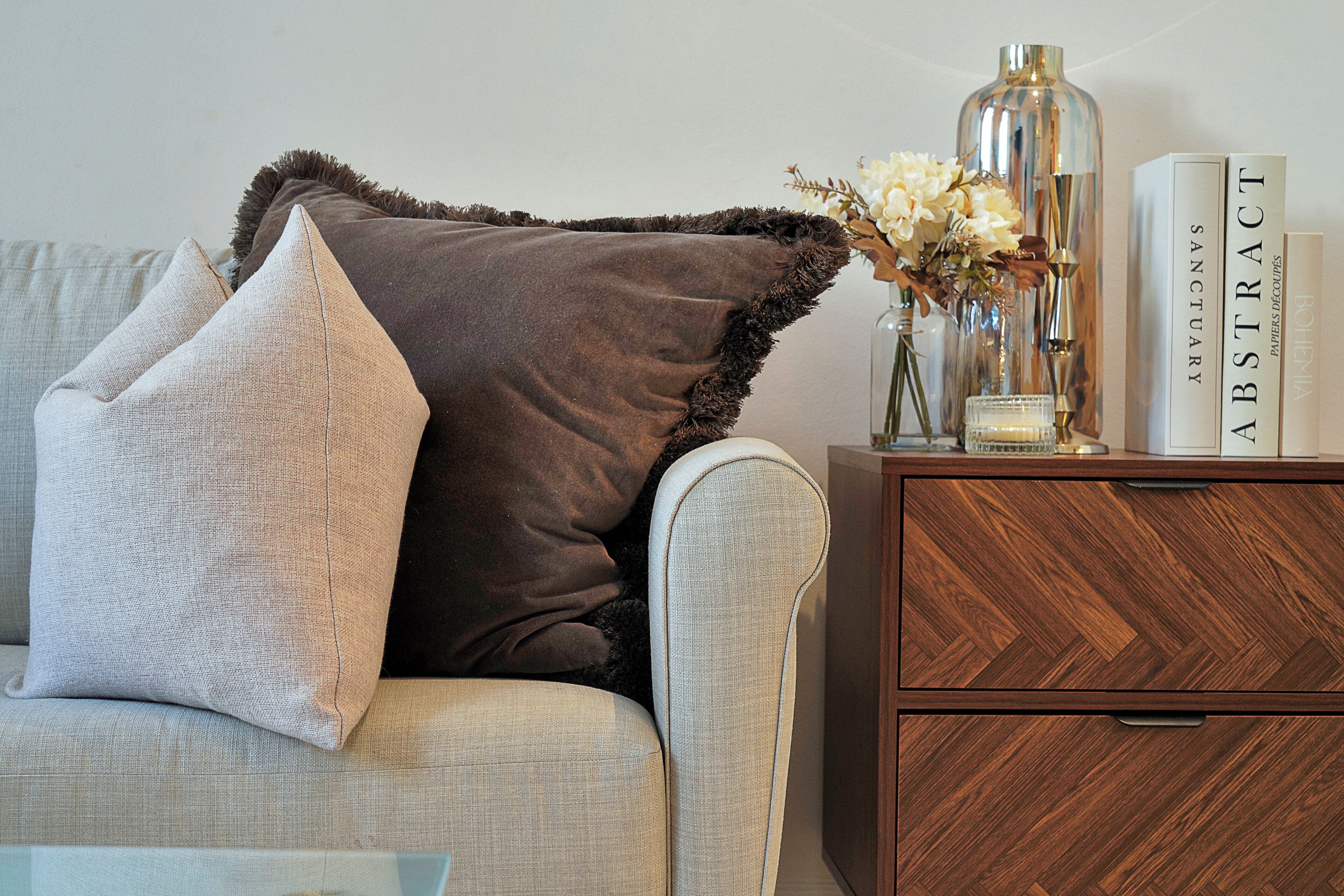 A living room with a sofa, pillows, a vase with flowers, and a wooden side table with books.