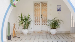 A white door with decorative metalwork, potted plants, and a tiled floor. - Pousada Maria Maria (Salvador)