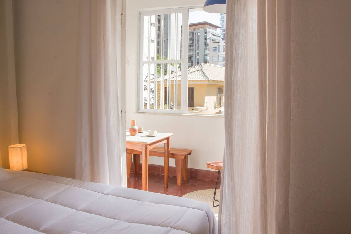 A bedroom with a bed, a window, a table, and a chair.
