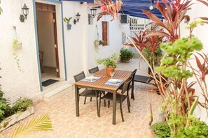 Une terrasse avec une table et des chaises, des plantes en pot et une porte donnant sur un espace intérieur.