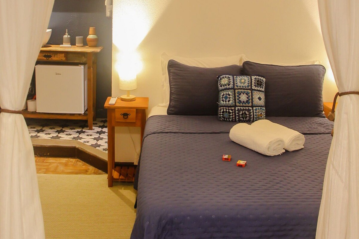 A bedroom with a bed, bedside table, lamp, and curtains.