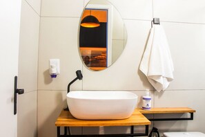 A bathroom with a white sink, a mirror, a towel hanging on a rack, and a bottle of hand soap. - Pousada Maria Maria (Salvador)