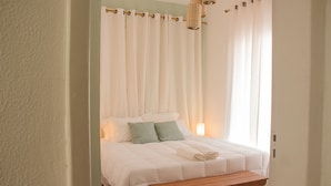 A bedroom with a bed, pillows, a bedside table, and curtains. - Pousada Maria Maria (Salvador)