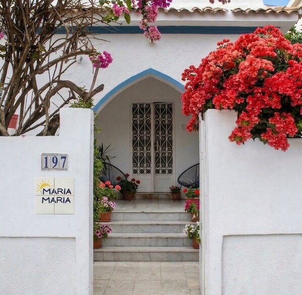 Un bâtiment blanc avec une porte bleue, portant le numéro 197, et une enseigne sur laquelle on peut lire « MARIA MARIA ».