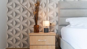 A neatly made bed with a headboard, a bedside table with a lamp, and a decorative wall panel. - Saranda Bay Retreat - 1BR Apartment (Sarandë)