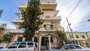 A multi-story residential building with a central entrance, balconies on each floor, and a tree in front. - Saranda Bay Retreat - 1BR Apartment (Sarandë)