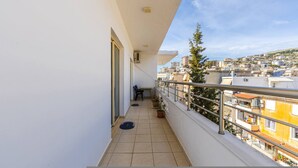 A narrow balcony with a view of a cityscape, a potted plant, and a chair. - Saranda Bay Retreat - 1BR Apartment (Sarandë)