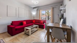 A modern living room with a red sectional sofa, a wooden coffee table, and a dining table with chairs. - Saranda Bay Retreat - 1BR Apartment (Sarandë)