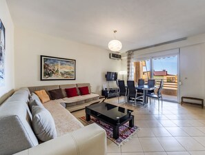 Ein modernes Wohnzimmer mit einer Couch, einem Couchtisch, einem Fernseher und einem Essbereich mit Stühlen und einem Tisch.