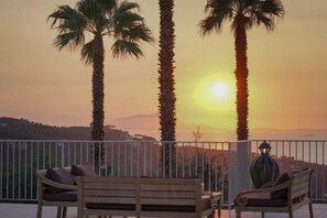 A balcony with two wooden benches and a metal railing, overlooking a sunset with palm trees and distant hills. - Villa Kalisa- Hillside Heritage Villa just steps from Sorrento Centre (Sorrento)