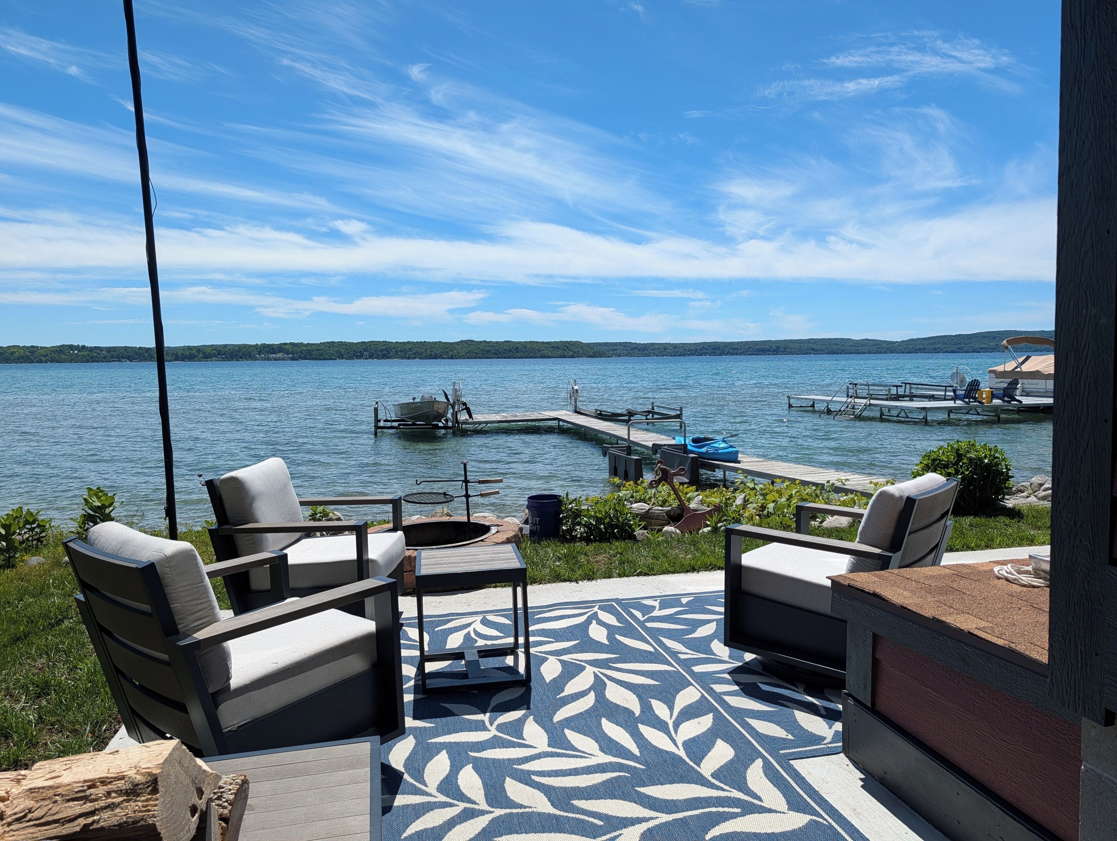 A deck with outdoor furniture overlooking a lake, dock with boats, and a clear sky.