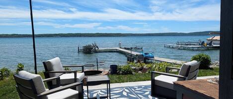 A deck with outdoor furniture overlooking a lake, dock with boats, and a clear sky.