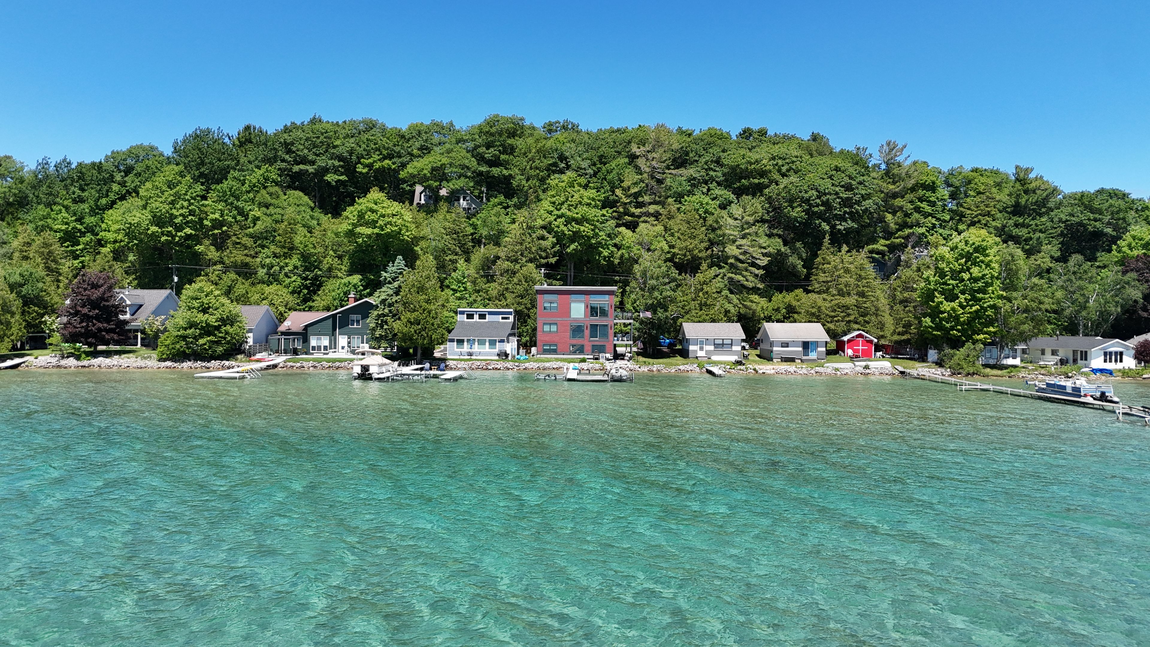 A lakeside property with clear water, docked boats, and a forested hill in the background.
