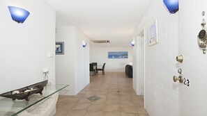 A hallway with a glass table displaying decorative items, a dining area with a table and chairs, and a view of the sea through a window. - Quarterdeck 23 - Stunning Ocean Views (Lennox Head)