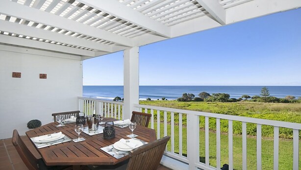 Un área de comedor al aire libre techada con una mesa dispuesta para dos, con vistas a un paisaje costero.
