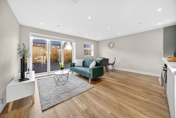 A modern living room with a green sofa, a white side table, and a grey rug. - Cosy 2BR - Fast Wi-Fi - Work Space - Free Parking (Cardiff)