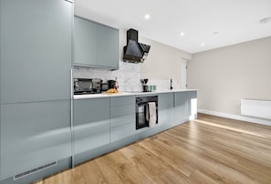 A modern kitchen with grey cabinets, a black range hood, and a built-in oven. - Cosy 2BR - Fast Wi-Fi - Work Space - Free Parking (Cardiff)