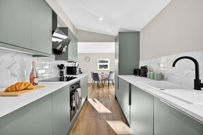 A modern kitchen with a central island, a dining area with chairs, and a view of the outdoors. - 2BR - Fast Wi-Fi - Work Space - Free Parking (Cardiff)