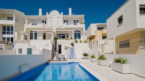 Un bâtiment moderne de couleur blanche, doté d’une piscine au centre, et entouré de balcons et de plantes en pot.