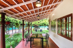 Un espacio exterior cubierto para comer con mesa y sillas, rodeado de vegetación y vistas a un jardín paisajístico.