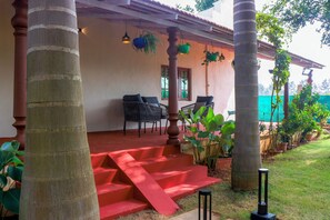 A covered outdoor area with a red staircase leading to a seating area with chairs and tables. - Alaya Stays Eco Serenity 2-BHK With Pool (Doddaballapur)