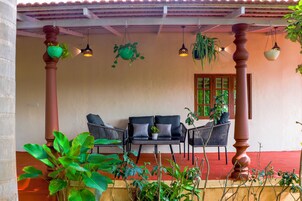 Un espacio de estar al aire libre techado, con piso rojo, dos sofás y plantas colgantes.
