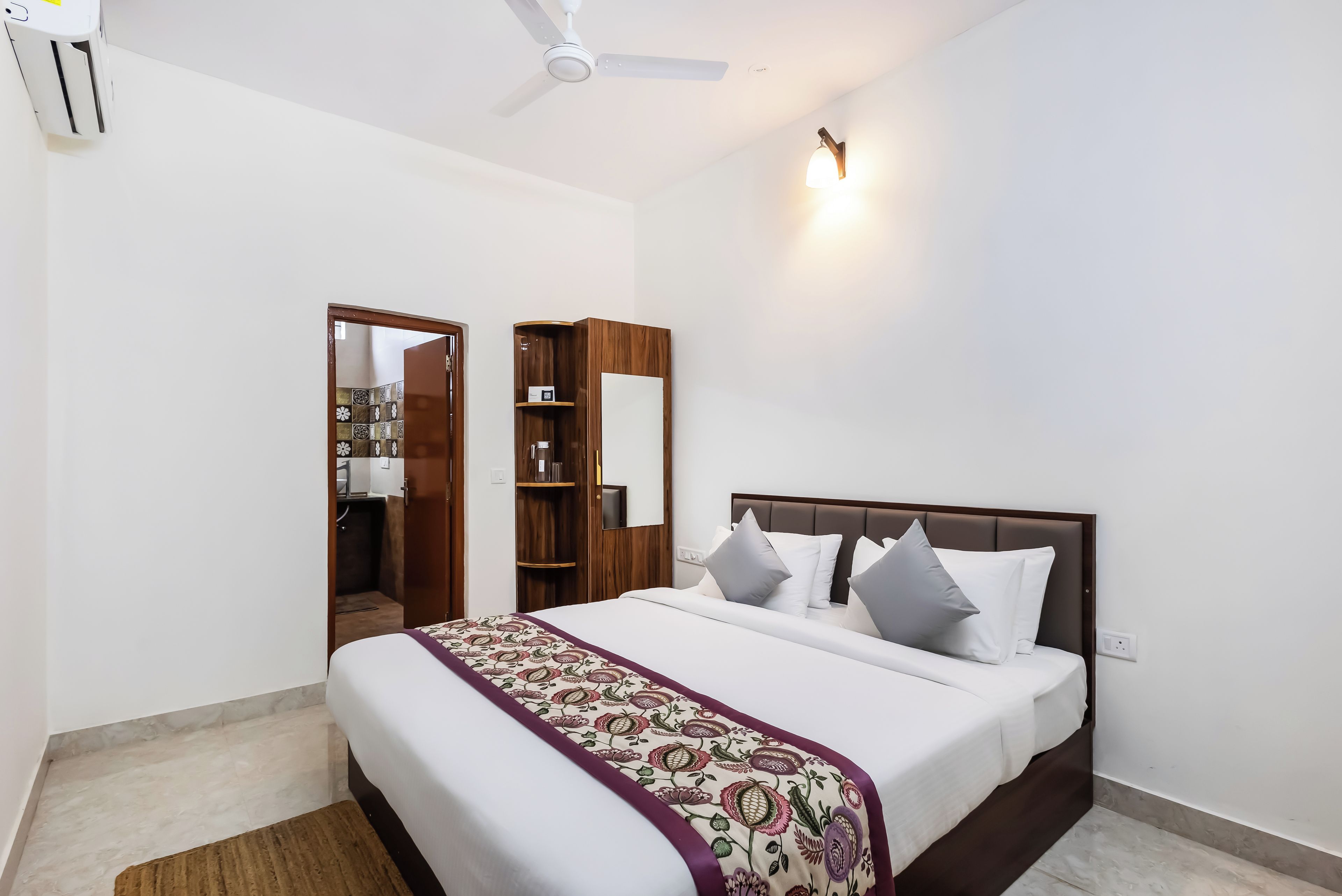 A bedroom with a bed, bedside tables, a wardrobe, a ceiling fan, and a wall-mounted light fixture.