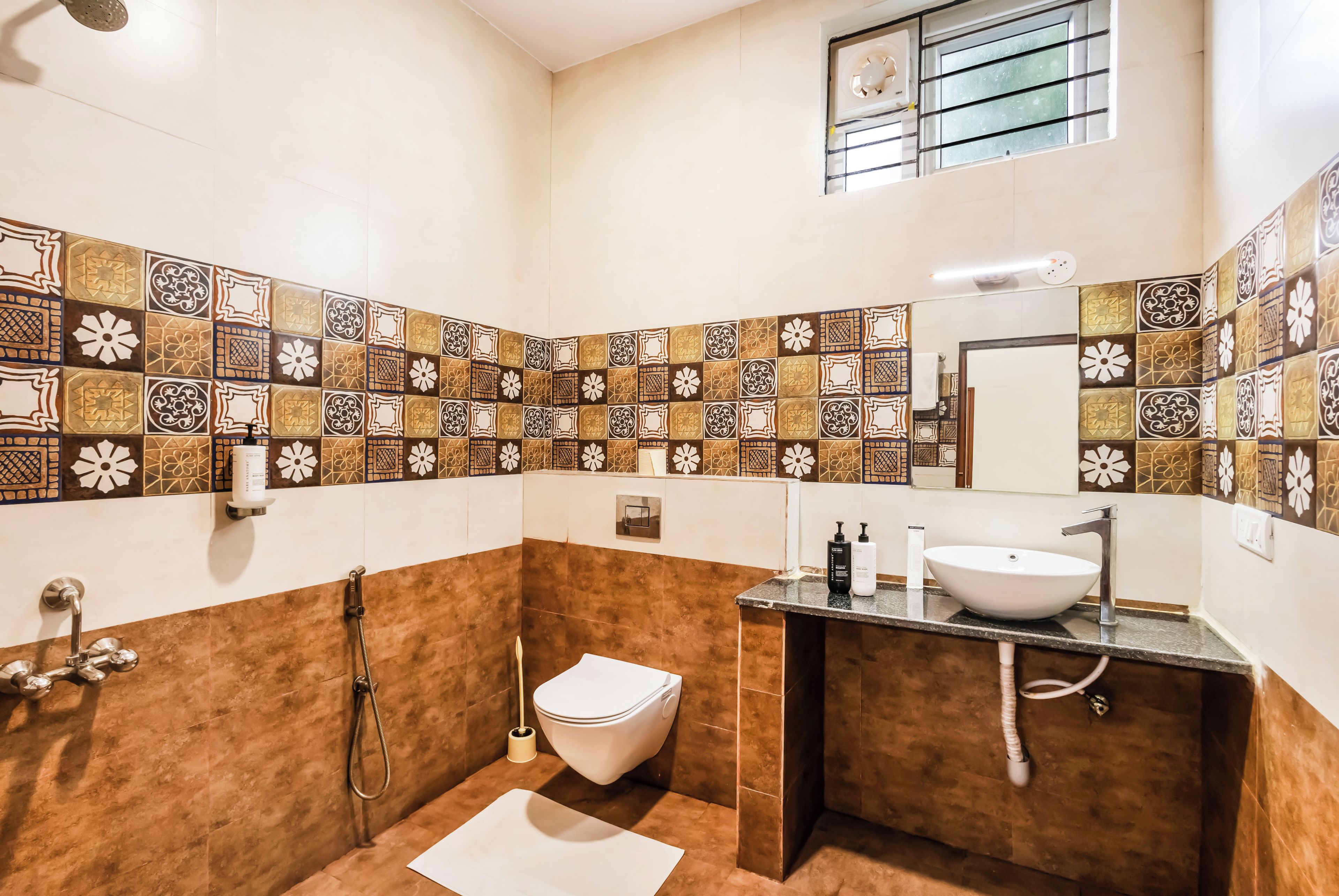 A bathroom with a white toilet, a sink, and a shower. The walls are decorated with patterned tiles.