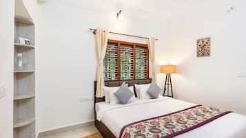 A bedroom with a bed, a bedside lamp, a window with curtains, a shelf with items, and a wall-mounted picture.