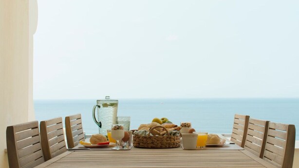Une table dressée pour le petit-déjeuner, avec des chaises et une vue sur la mer.
