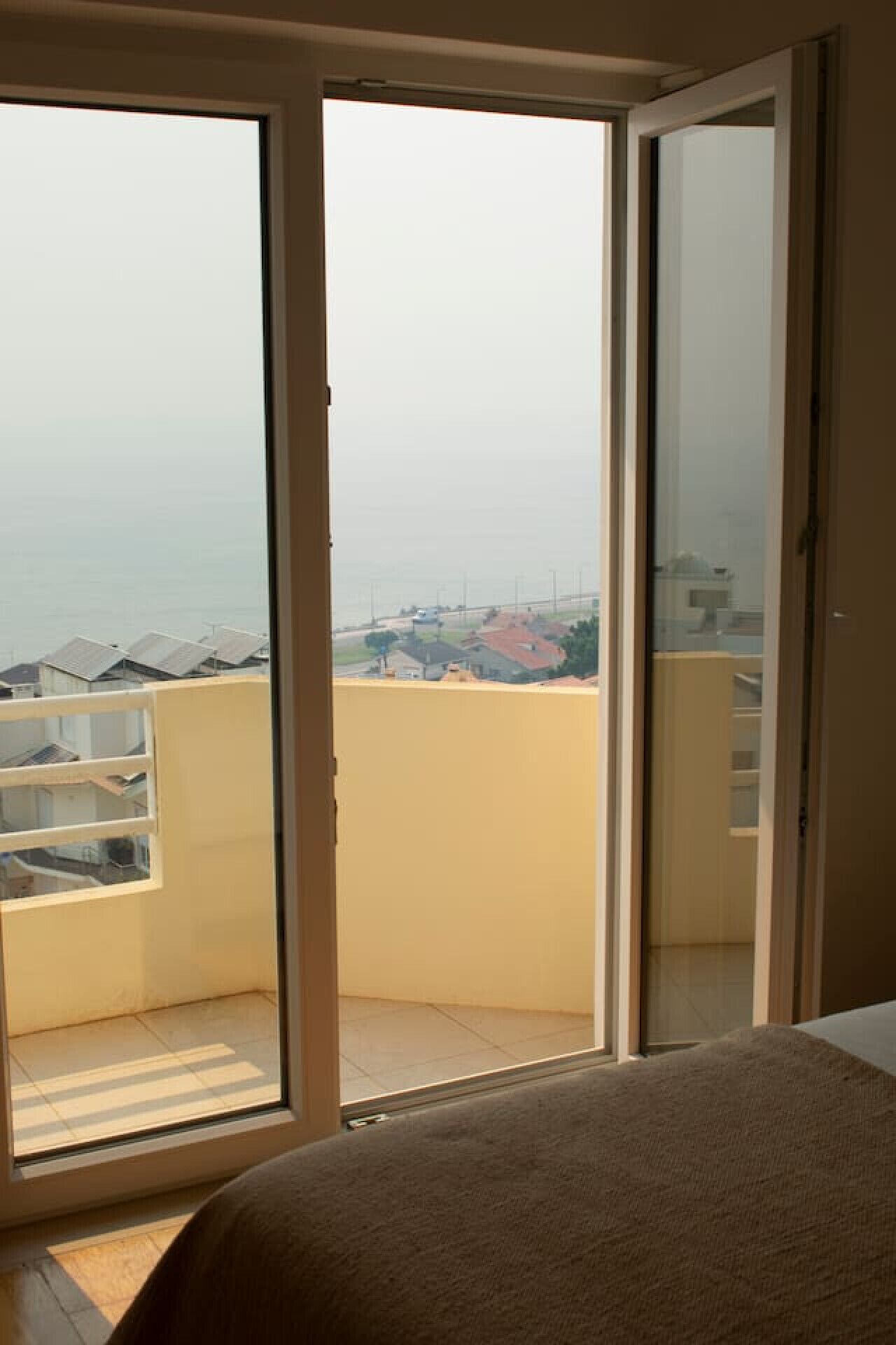 A room with a large sliding glass door leading to a balcony. The balcony has a view of a residential area with houses and a clear sky.